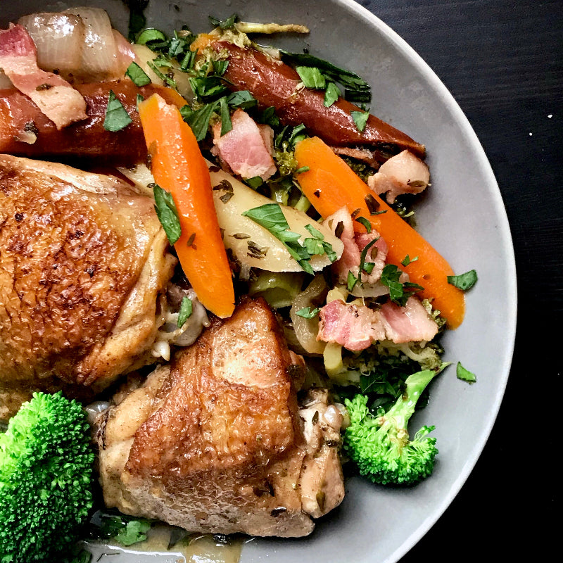 Bowl of chicken and vegetable stew with carrots, broccoli, and onions on a dark surface