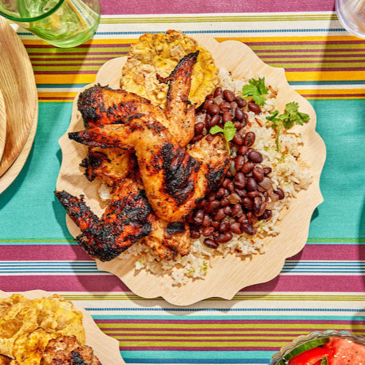 Plated dish with grilled chicken, beans, and rice on a colorful striped tablecloth.