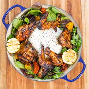 Bowl of grilled chicken wings with lemon slices and salad on a wooden surface